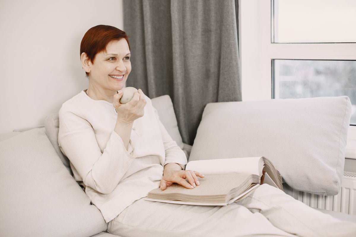 Frau mit einer Tasse und einem aufgeschlagenen Buch auf dem Sofa
