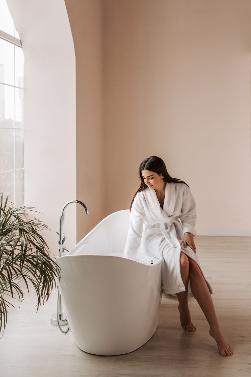 Frau im weißen Bademantel sitzt an einer Badewanne