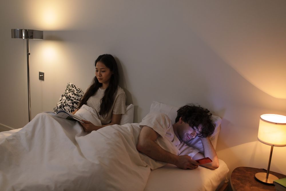 Ein Paar im Bett: eine Person liest, die andere benutzt ein Smartphone
