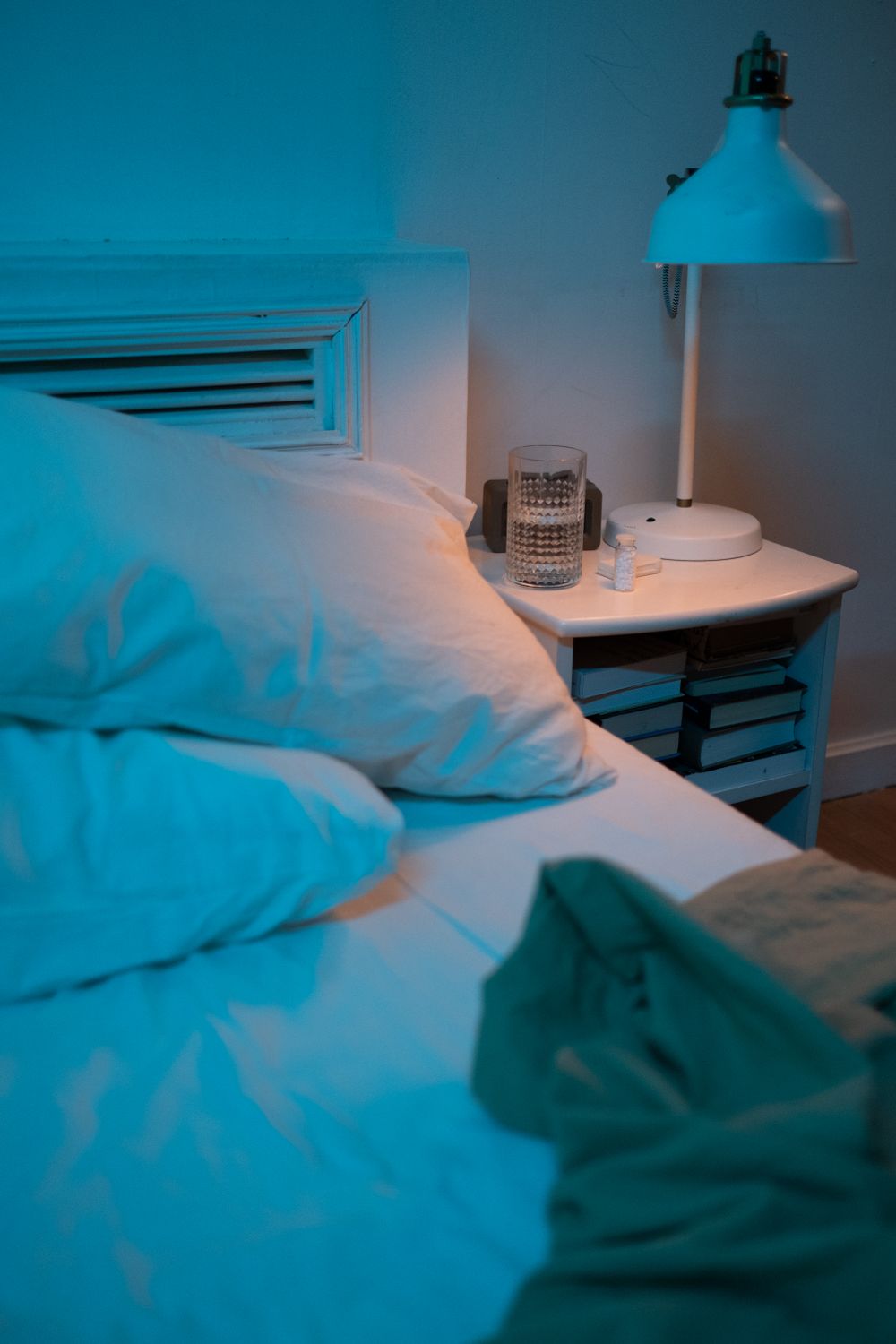 Nachttisch mit Lampe und Wasserglas neben einem Bett