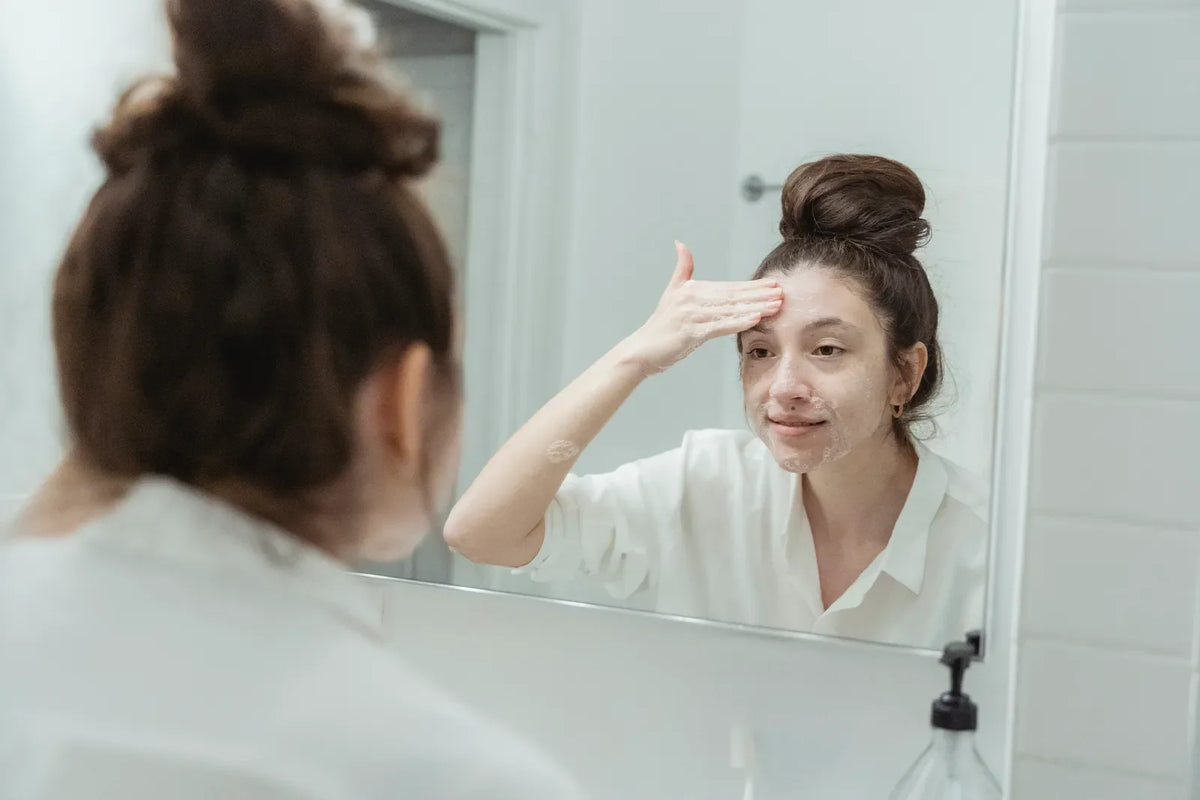 Eine Frau trägt Gesichtspflege vor dem Spiegel auf. Foto: Miriam Alonso / Pexels.