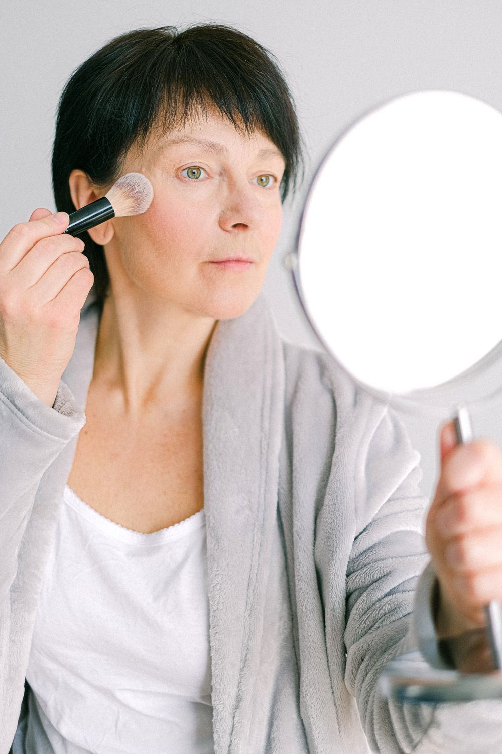 Frau trägt mit einem Pinsel Make-up vor einem Spiegel auf